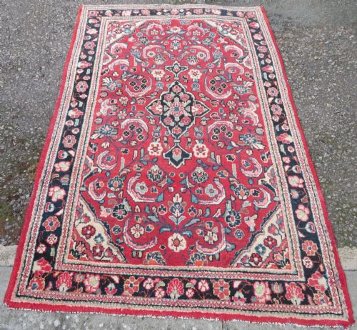 fig 1. An antique West Persian Mahal rug featuring a red ground, central navy medallion, floral spandrels, and a decorative border.