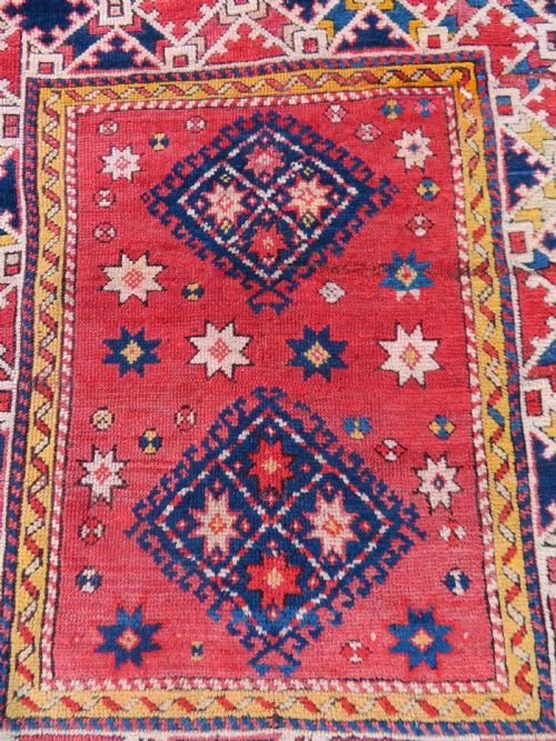 fig 1. An antique hand-knotted wool rug featuring geometric diamond medallions in red, dark blue, yellow, and cream with a detailed border pattern.