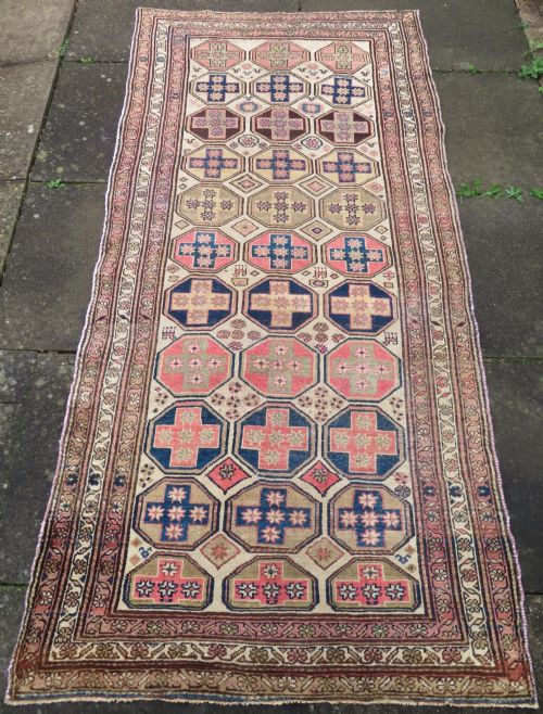 fig 1. An antique hand-knotted Kurdish runner rug featuring repeating octagonal geometric medallions in pink, indigo, and cream tones.