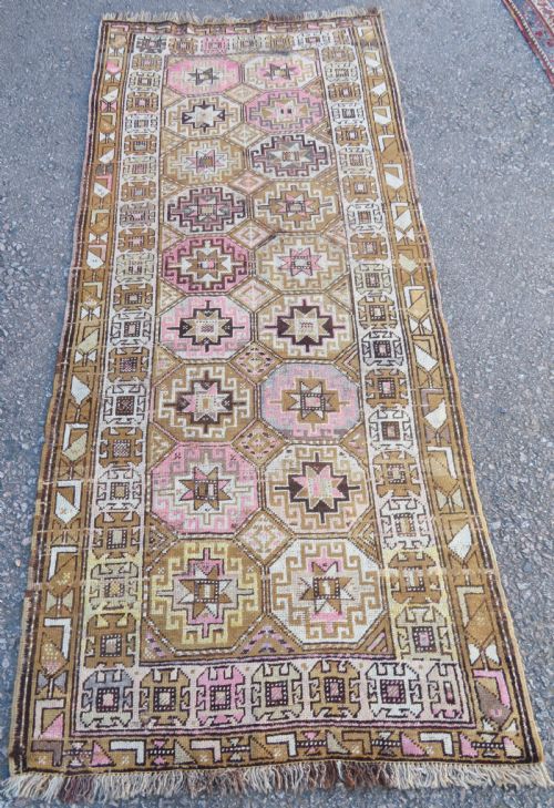 fig 1. An antique Kurdish hand-knotted wool rug runner featuring repeated geometric octagonal medallions in shades of pink, tan, cream, and dark brown.