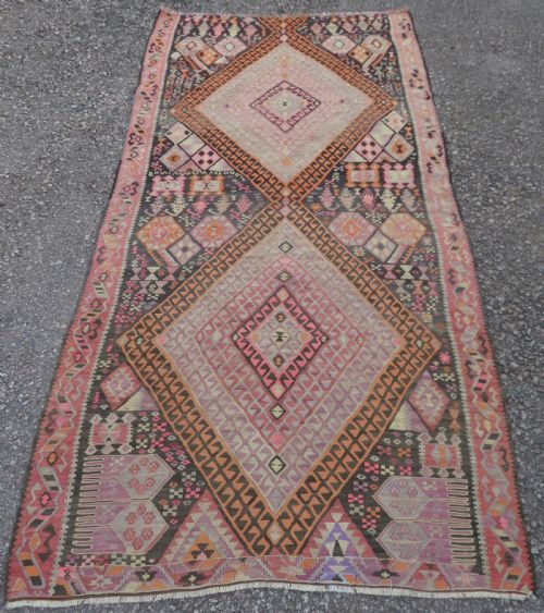 fig 1. An antique flatwoven Turkish kilim rug featuring central diamond medallions and geometric borders in shades of pink, terracotta, cream, and dark brown.