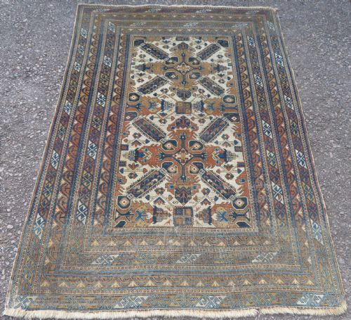 fig 1. An antique hand-knotted Caucasian Kuba Seichur wool rug featuring a geometric white ground field surrounded by multi-layered patterned borders in blue, terracotta, and ochre.