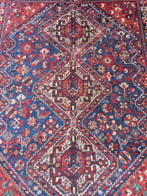 fig 1. An antique South Persian Khamseh rug featuring three diamond-shaped central medallions and geometric bird motifs in shades of red, navy blue, and cream.