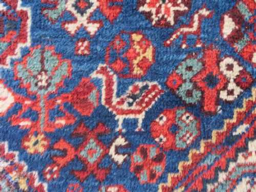 fig 2. An antique South Persian Khamseh rug featuring three diamond-shaped central medallions and geometric bird motifs in shades of red, navy blue, and cream.