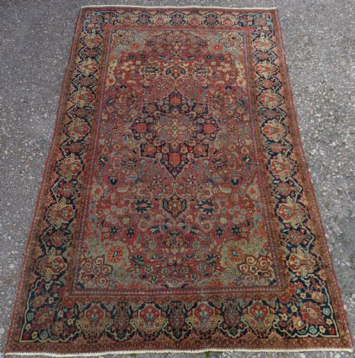 fig 1. A rectangular hand-knotted wool Kashan rug featuring a central starburst medallion surrounded by dense floral patterns on a terracotta field with a navy border.