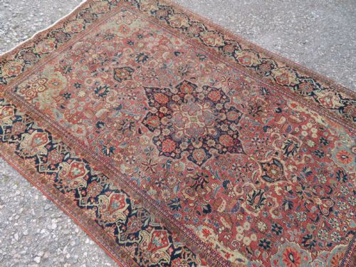 fig 2. A rectangular hand-knotted wool Kashan rug featuring a central starburst medallion surrounded by dense floral patterns on a terracotta field with a navy border.