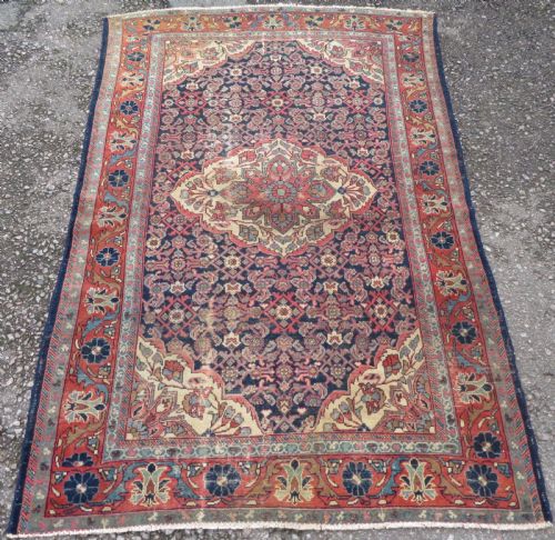 fig 1. A rectangular antique Persian Malayer wool rug with a central cream and red medallion set against a dark navy field surrounded by intricate floral borders.
