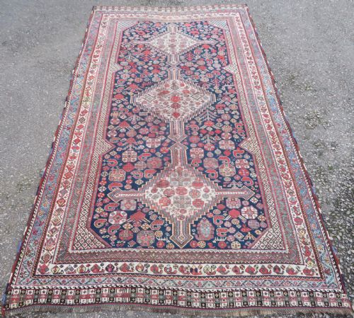 fig 1. An antique hand-knotted Khamseh tribal wool rug featuring three geometric pole medallions in navy blue, terracotta red, and cream with detailed borders.