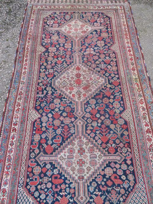fig 2. An antique hand-knotted Khamseh tribal wool rug featuring three geometric pole medallions in navy blue, terracotta red, and cream with detailed borders.