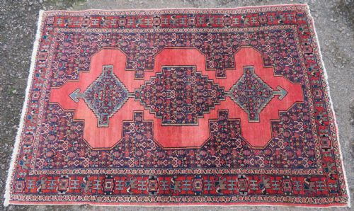 fig 1. An antique West Persian Senneh wool rug featuring a navy blue stepped diamond medallion centered on a terracotta red field with intricate geometric borders.