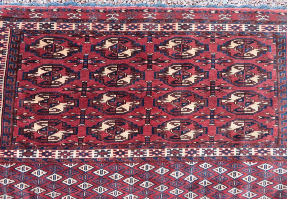 A rectangular hand-knotted Yomut Turkmen chuval rug featuring repeating gul motifs on a deep red field with a geometric border and diamond-patterned lower elem. View II