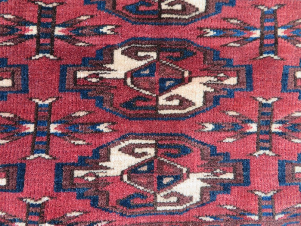 A rectangular hand-knotted Yomut Turkmen chuval rug featuring repeating gul motifs on a deep red field with a geometric border and diamond-patterned lower elem. View III