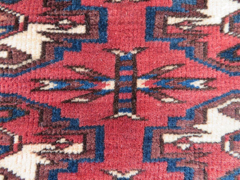 A rectangular hand-knotted Yomut Turkmen chuval rug featuring repeating gul motifs on a deep red field with a geometric border and diamond-patterned lower elem. View IV