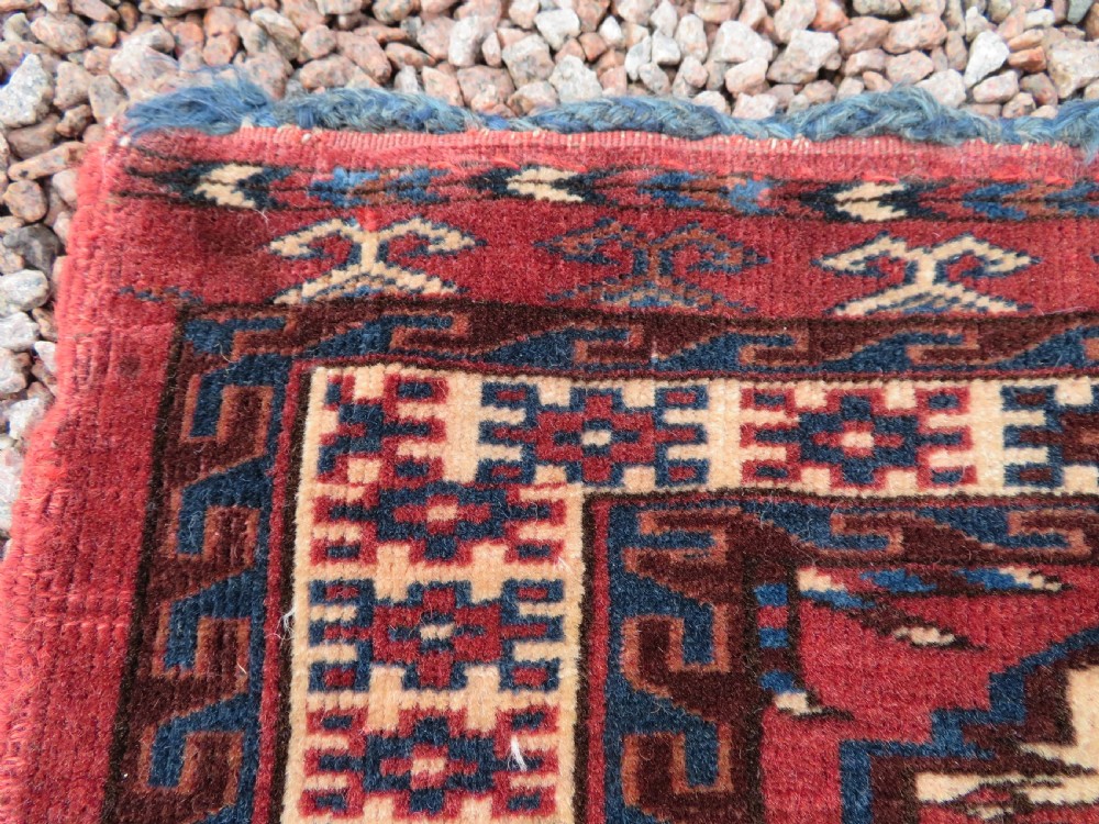 A rectangular hand-knotted Yomut Turkmen chuval rug featuring repeating gul motifs on a deep red field with a geometric border and diamond-patterned lower elem. View V