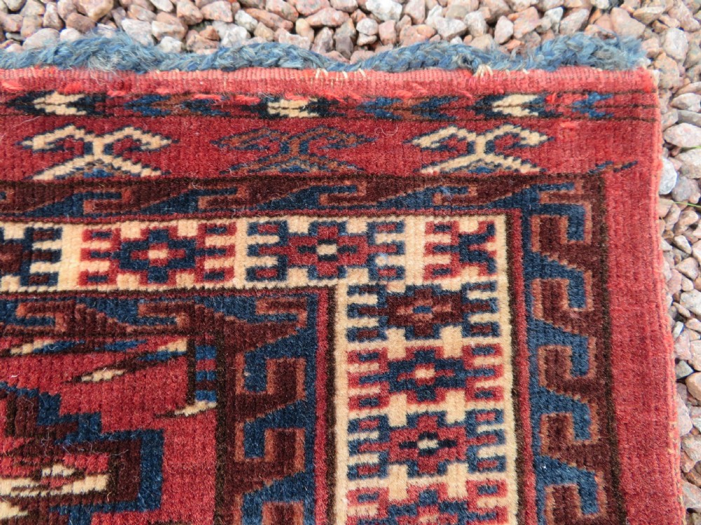 A rectangular hand-knotted Yomut Turkmen chuval rug featuring repeating gul motifs on a deep red field with a geometric border and diamond-patterned lower elem. View VI