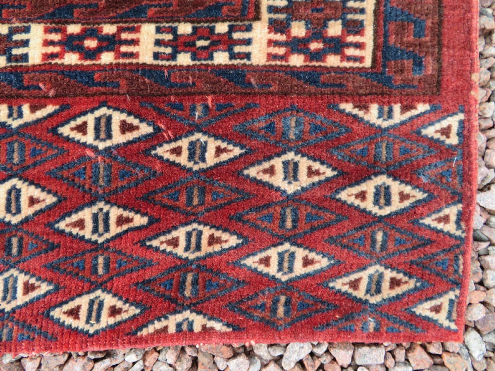 A rectangular hand-knotted Yomut Turkmen chuval rug featuring repeating gul motifs on a deep red field with a geometric border and diamond-patterned lower elem. View VII