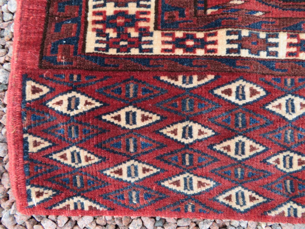 A rectangular hand-knotted Yomut Turkmen chuval rug featuring repeating gul motifs on a deep red field with a geometric border and diamond-patterned lower elem. View VIII