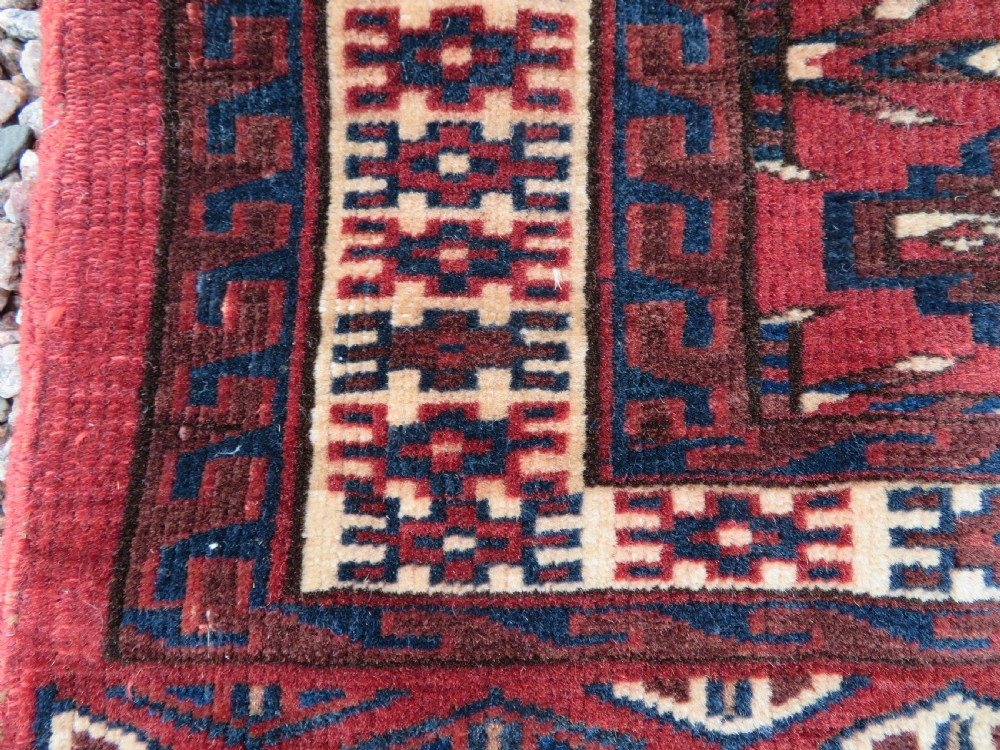A rectangular hand-knotted Yomut Turkmen chuval rug featuring repeating gul motifs on a deep red field with a geometric border and diamond-patterned lower elem. View IX