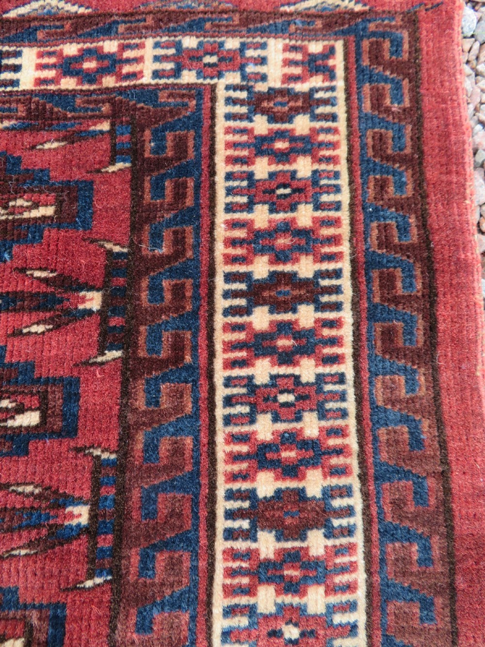 A rectangular hand-knotted Yomut Turkmen chuval rug featuring repeating gul motifs on a deep red field with a geometric border and diamond-patterned lower elem. View X
