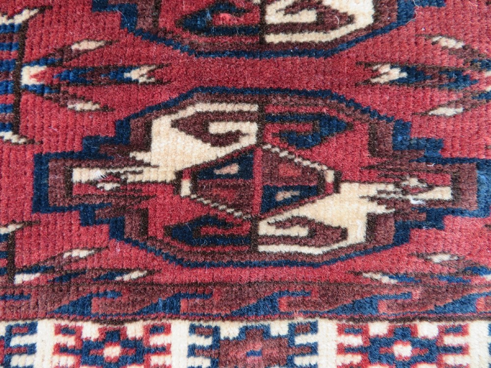A rectangular hand-knotted Yomut Turkmen chuval rug featuring repeating gul motifs on a deep red field with a geometric border and diamond-patterned lower elem. View XI
