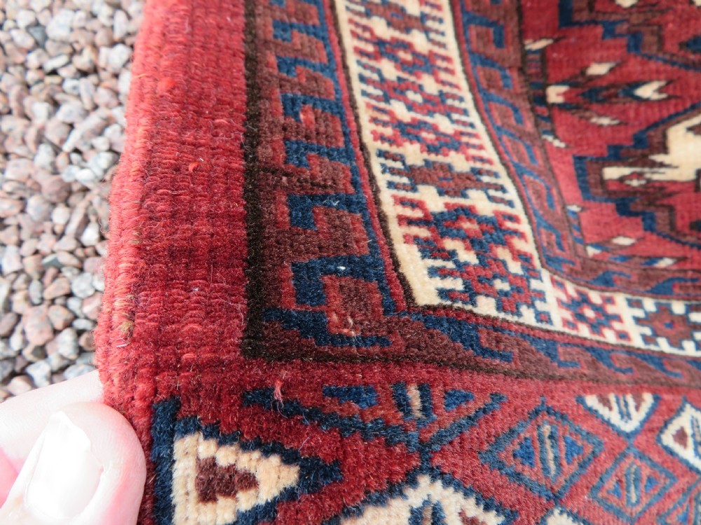 A rectangular hand-knotted Yomut Turkmen chuval rug featuring repeating gul motifs on a deep red field with a geometric border and diamond-patterned lower elem. View XII