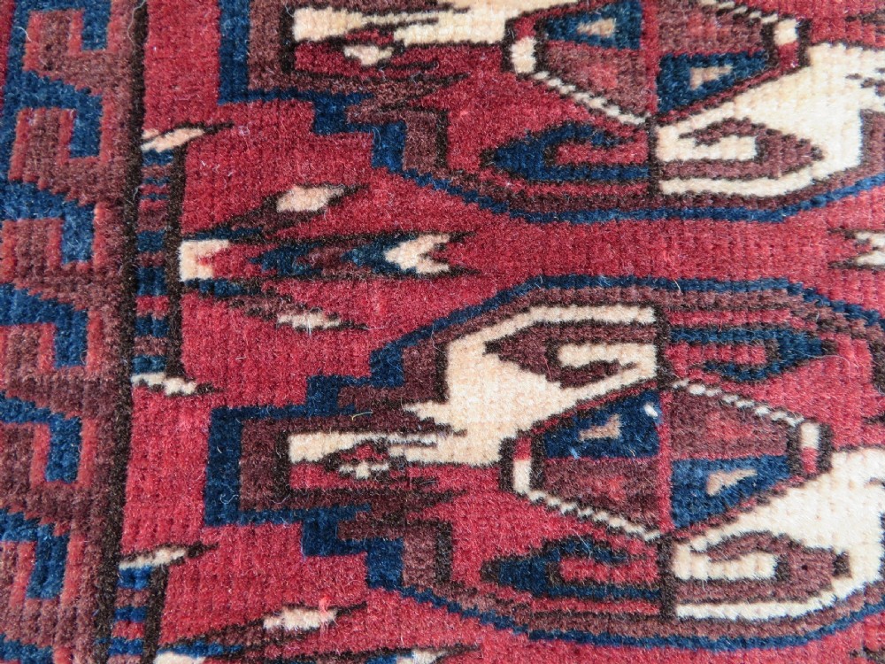 A rectangular hand-knotted Yomut Turkmen chuval rug featuring repeating gul motifs on a deep red field with a geometric border and diamond-patterned lower elem. View XIII