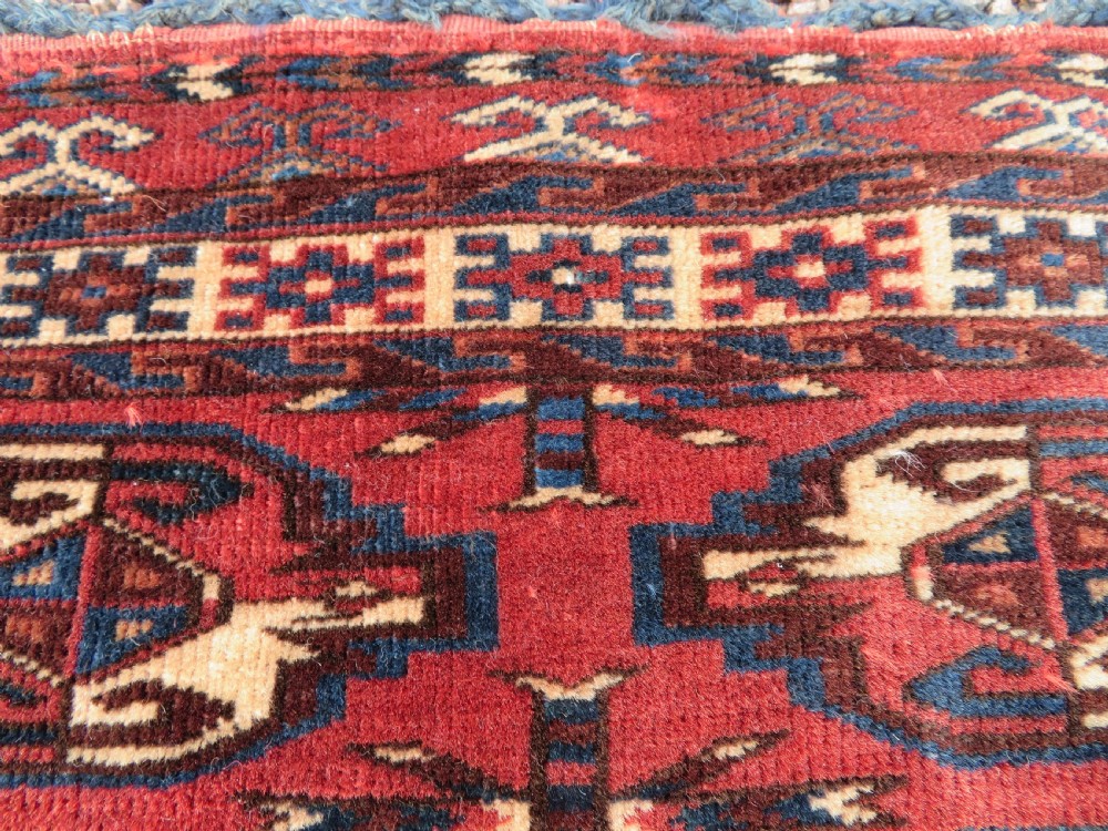A rectangular hand-knotted Yomut Turkmen chuval rug featuring repeating gul motifs on a deep red field with a geometric border and diamond-patterned lower elem. View XIV