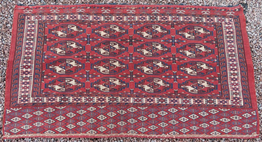 A rectangular hand-knotted Yomut Turkmen chuval rug featuring repeating gul motifs on a deep red field with a geometric border and diamond-patterned lower elem. View XV