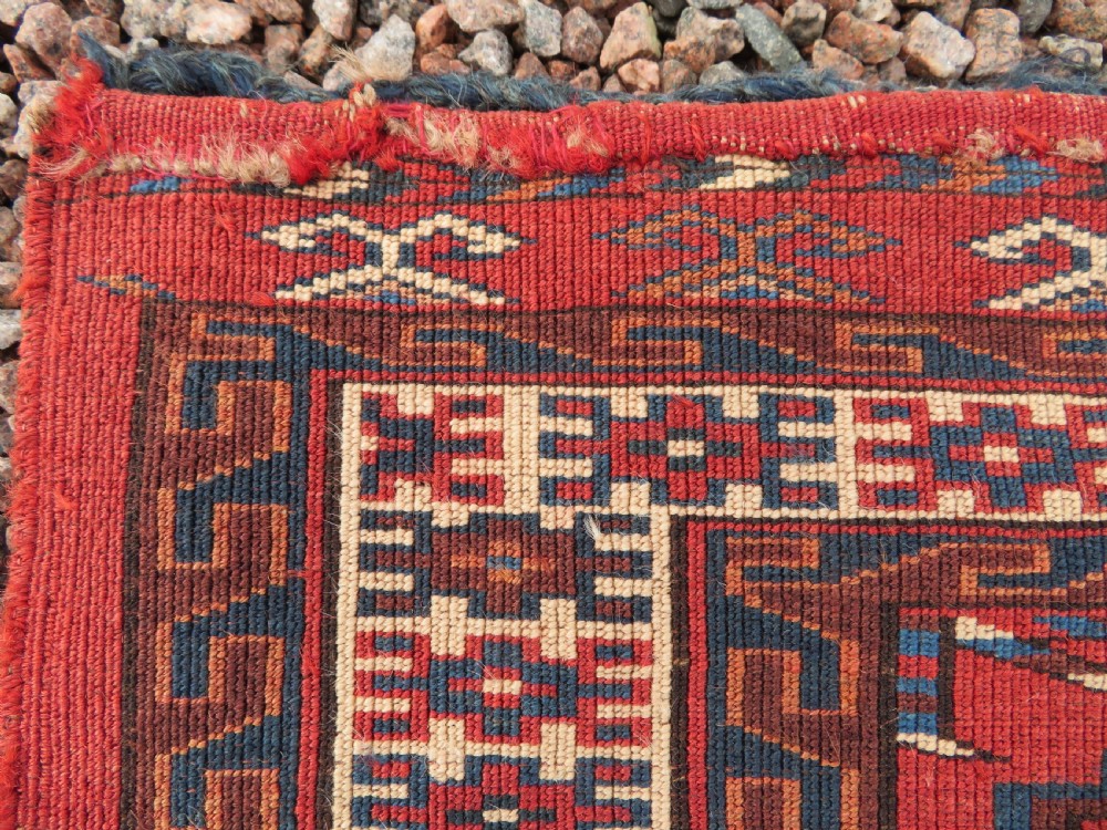 A rectangular hand-knotted Yomut Turkmen chuval rug featuring repeating gul motifs on a deep red field with a geometric border and diamond-patterned lower elem. View XVI