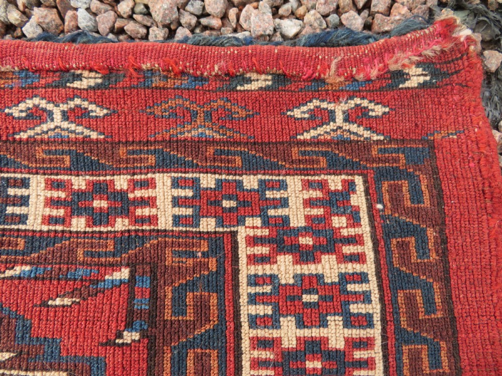A rectangular hand-knotted Yomut Turkmen chuval rug featuring repeating gul motifs on a deep red field with a geometric border and diamond-patterned lower elem. View XVII