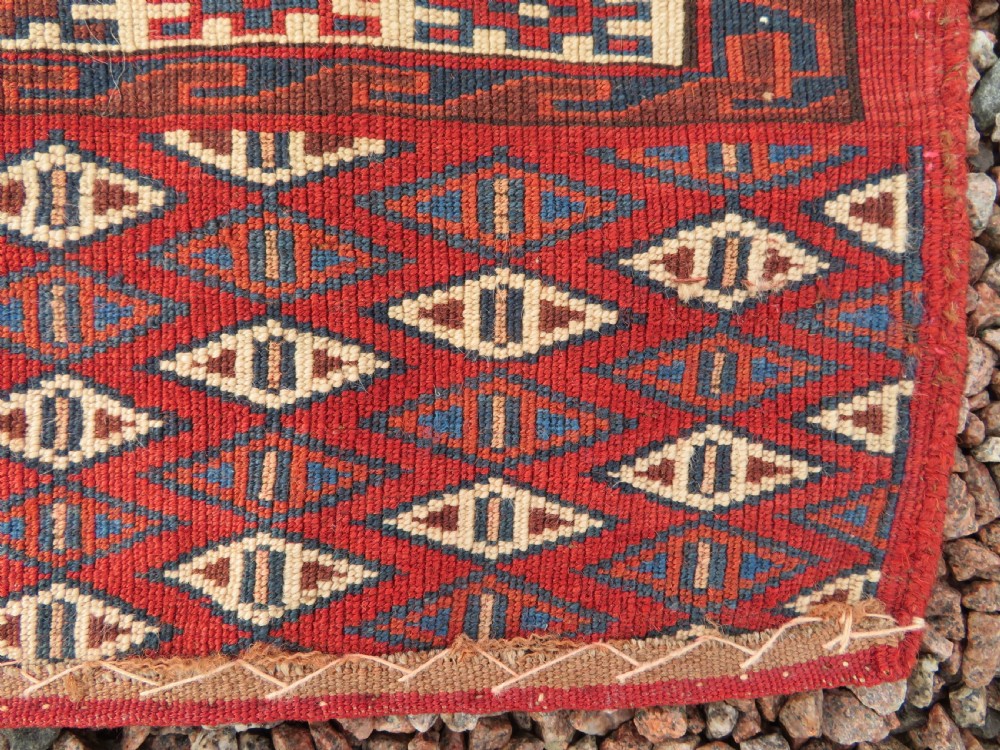 A rectangular hand-knotted Yomut Turkmen chuval rug featuring repeating gul motifs on a deep red field with a geometric border and diamond-patterned lower elem. View XVIII