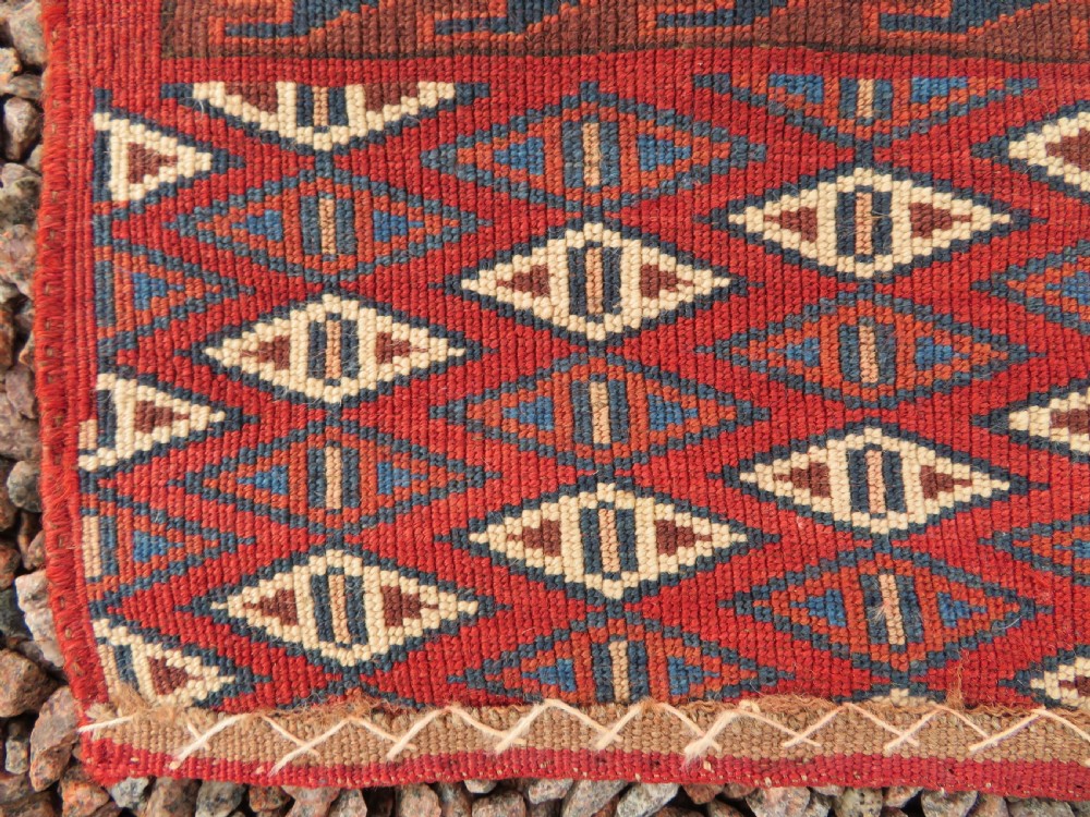 A rectangular hand-knotted Yomut Turkmen chuval rug featuring repeating gul motifs on a deep red field with a geometric border and diamond-patterned lower elem. View XIX