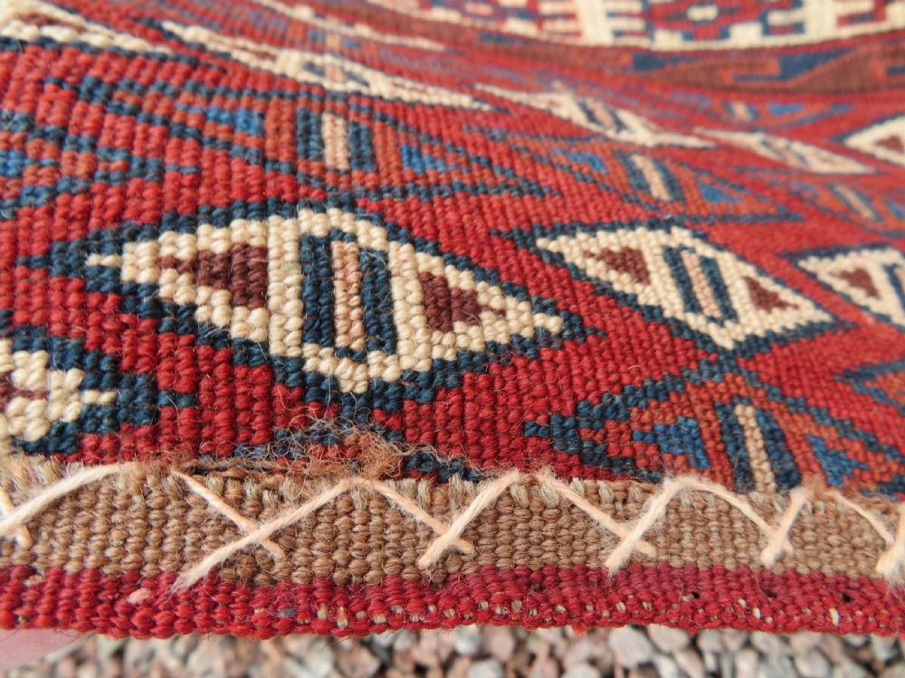 A rectangular hand-knotted Yomut Turkmen chuval rug featuring repeating gul motifs on a deep red field with a geometric border and diamond-patterned lower elem. View XXI