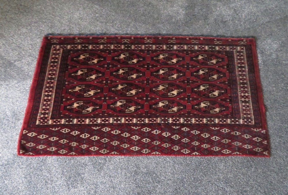 A rectangular hand-knotted Yomut Turkmen chuval rug featuring repeating gul motifs on a deep red field with a geometric border and diamond-patterned lower elem. View XXIII