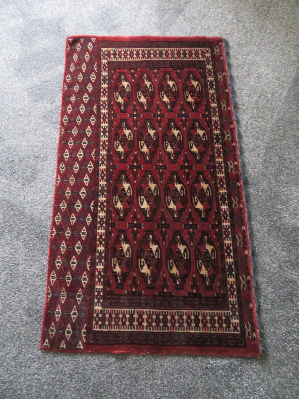 A rectangular hand-knotted Yomut Turkmen chuval rug featuring repeating gul motifs on a deep red field with a geometric border and diamond-patterned lower elem. View XXIV