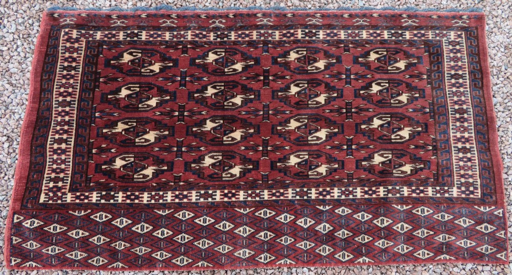 A rectangular hand-knotted Yomut Turkmen chuval rug featuring repeating gul motifs on a deep red field with a geometric border and diamond-patterned lower elem. View XXV