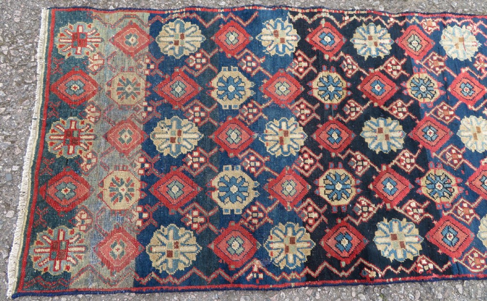 A long, narrow hand-knotted wool runner featuring a repeating geometric Mina Khana floral lattice pattern in navy blue, terracotta red, and cream tones. View III