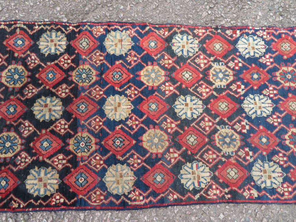 A long, narrow hand-knotted wool runner featuring a repeating geometric Mina Khana floral lattice pattern in navy blue, terracotta red, and cream tones. View IV