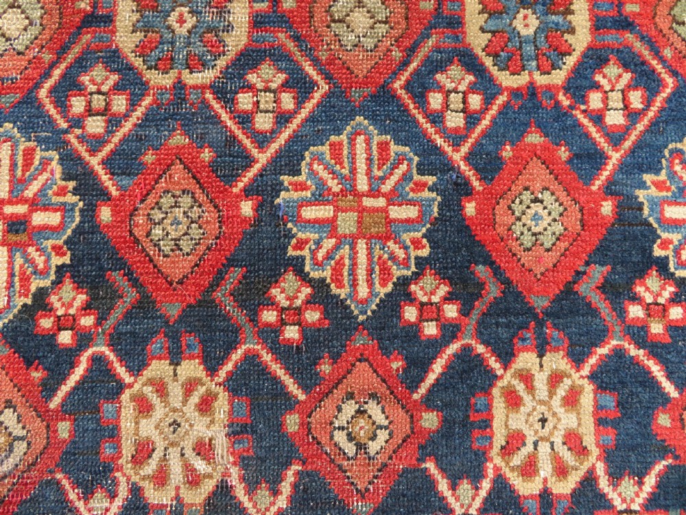 A long, narrow hand-knotted wool runner featuring a repeating geometric Mina Khana floral lattice pattern in navy blue, terracotta red, and cream tones. View VI