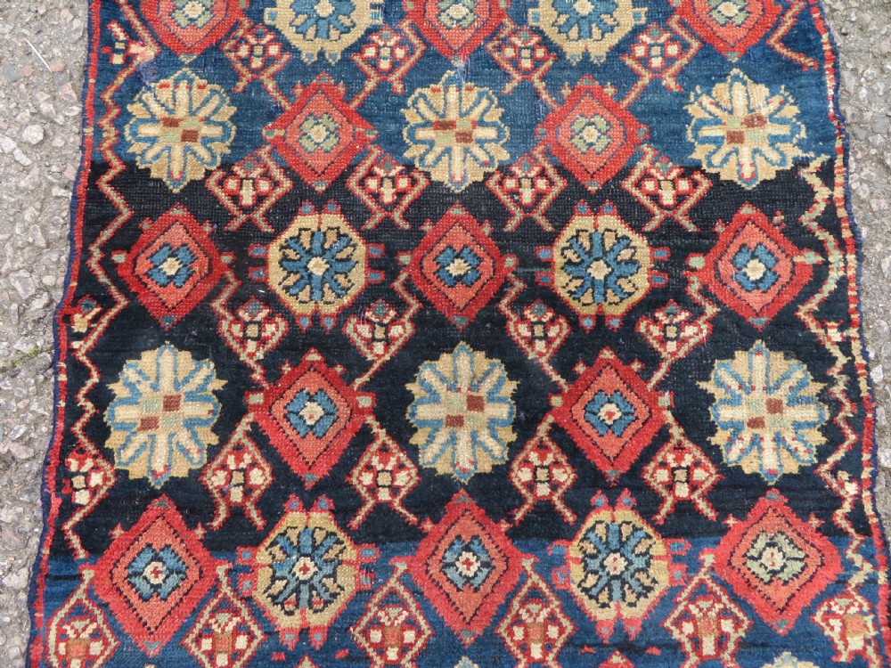 A long, narrow hand-knotted wool runner featuring a repeating geometric Mina Khana floral lattice pattern in navy blue, terracotta red, and cream tones. View VII
