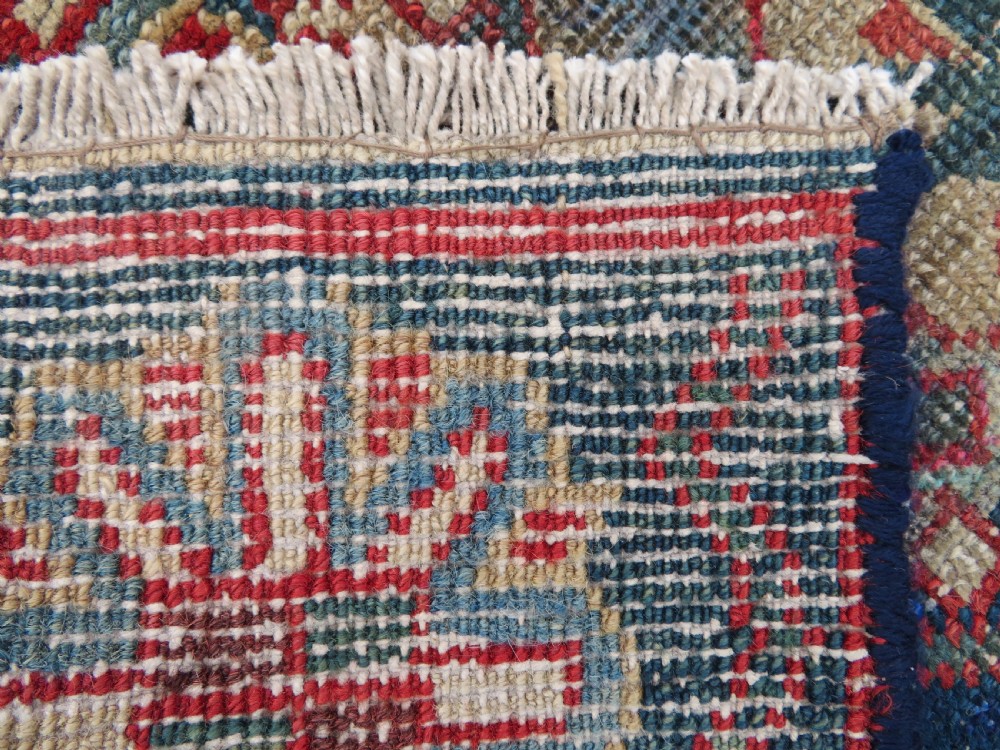 A long, narrow hand-knotted wool runner featuring a repeating geometric Mina Khana floral lattice pattern in navy blue, terracotta red, and cream tones. View X