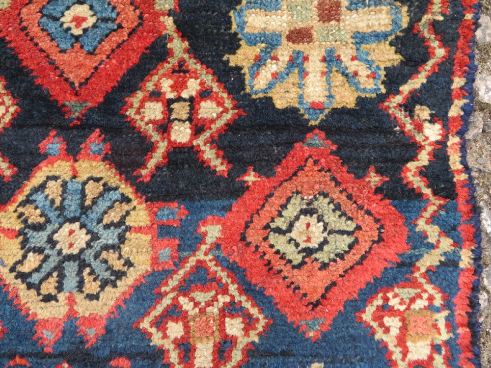 A long, narrow hand-knotted wool runner featuring a repeating geometric Mina Khana floral lattice pattern in navy blue, terracotta red, and cream tones. View XVII