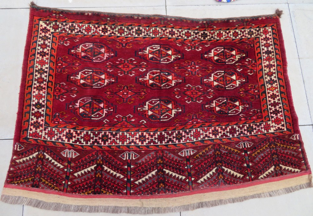 An antique woven Yomut Turkmen chuval rug in deep red wool featuring nine central geometric gul motifs surrounded by a patterned border and a detailed lower elem panel.