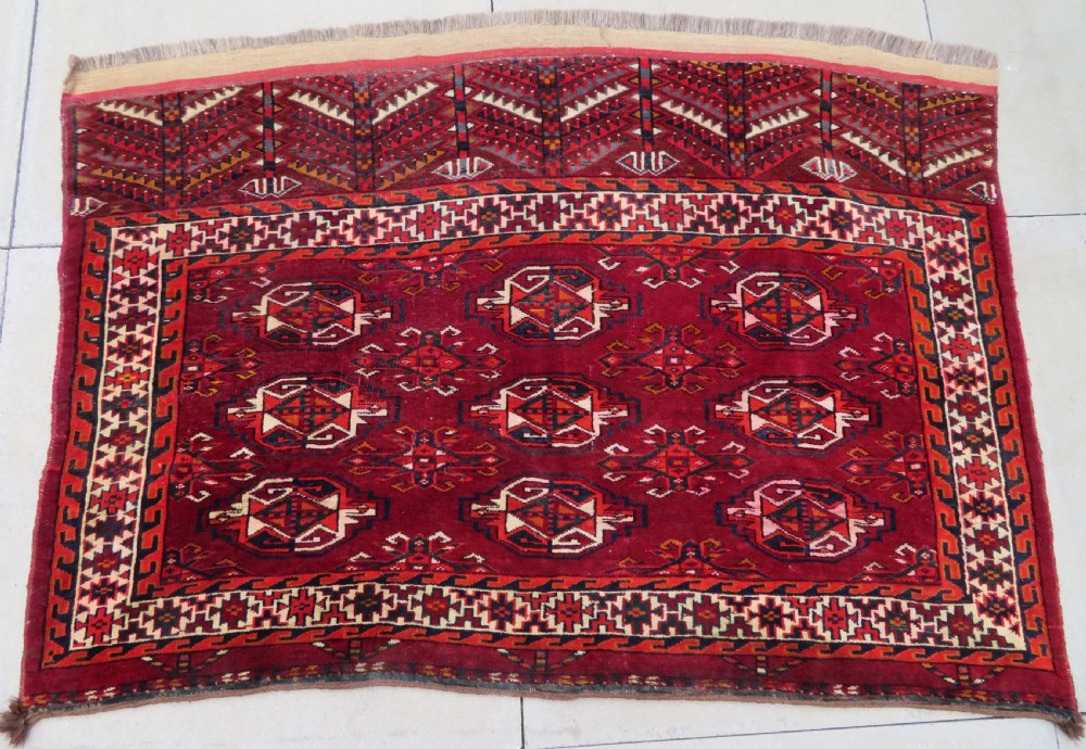 An antique woven Yomut Turkmen chuval rug in deep red wool featuring nine central geometric gul motifs surrounded by a patterned border and a detailed lower elem panel. View II
