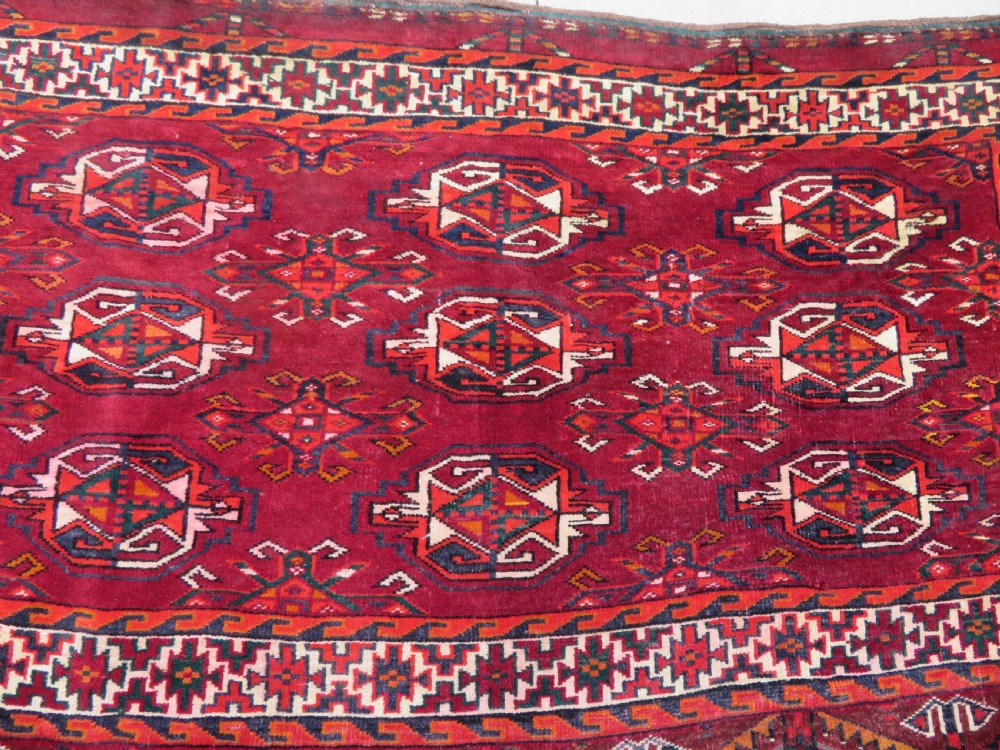 An antique woven Yomut Turkmen chuval rug in deep red wool featuring nine central geometric gul motifs surrounded by a patterned border and a detailed lower elem panel. View III
