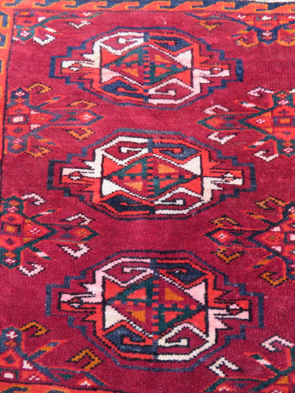 An antique woven Yomut Turkmen chuval rug in deep red wool featuring nine central geometric gul motifs surrounded by a patterned border and a detailed lower elem panel. View IV