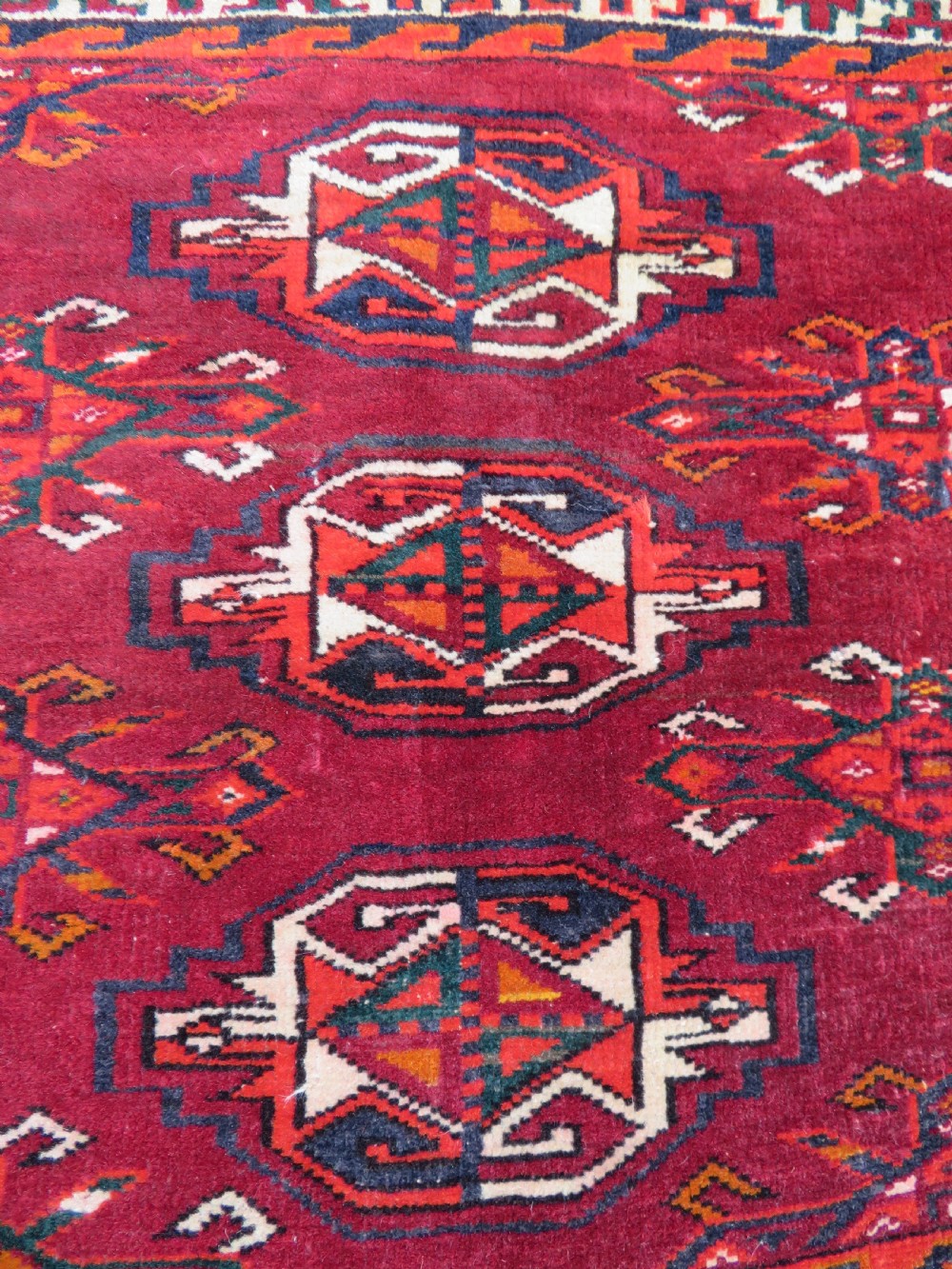An antique woven Yomut Turkmen chuval rug in deep red wool featuring nine central geometric gul motifs surrounded by a patterned border and a detailed lower elem panel. View V
