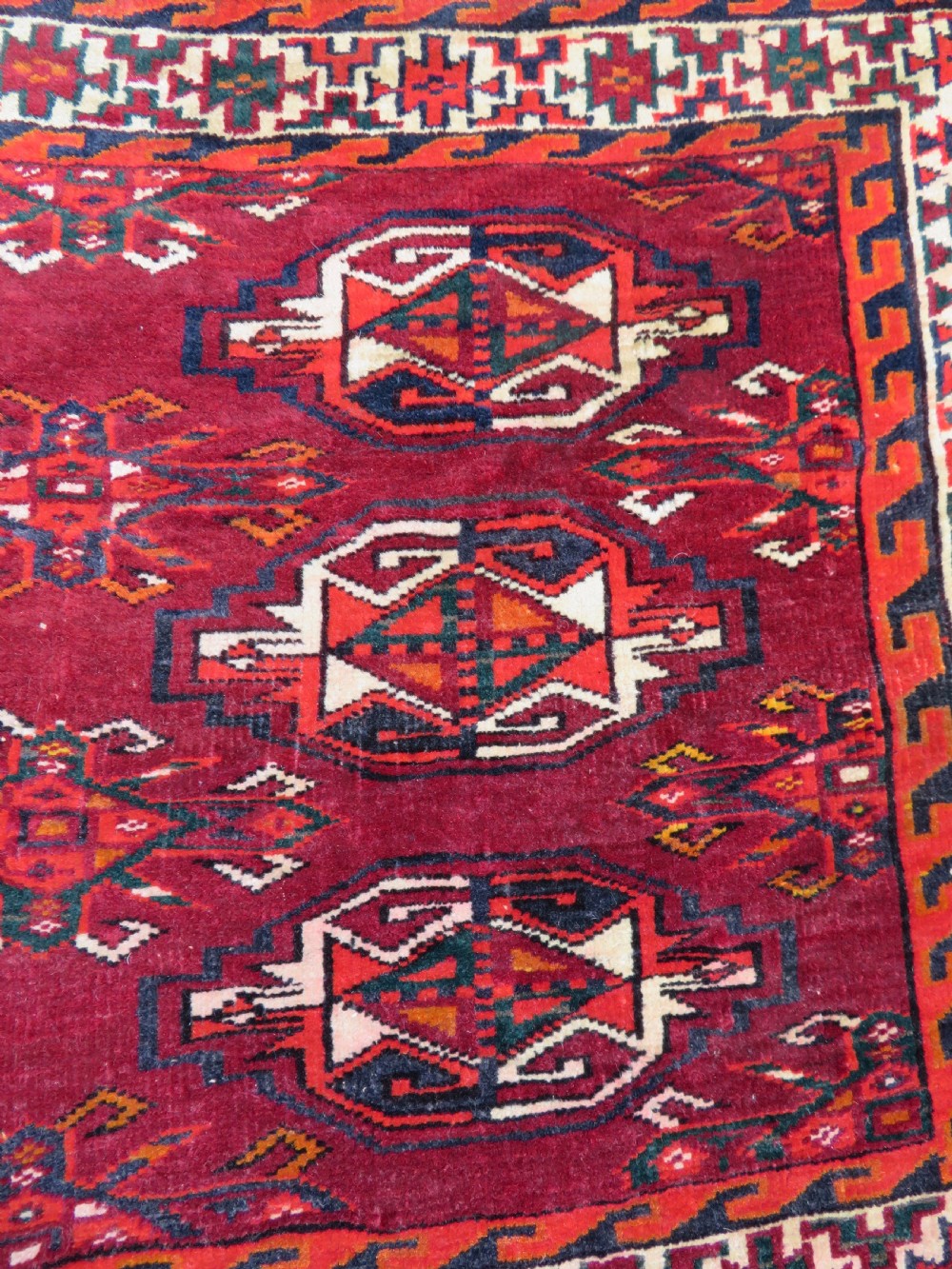 An antique woven Yomut Turkmen chuval rug in deep red wool featuring nine central geometric gul motifs surrounded by a patterned border and a detailed lower elem panel. View VI