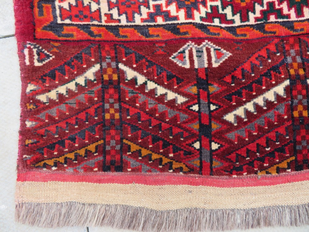 An antique woven Yomut Turkmen chuval rug in deep red wool featuring nine central geometric gul motifs surrounded by a patterned border and a detailed lower elem panel. View VII
