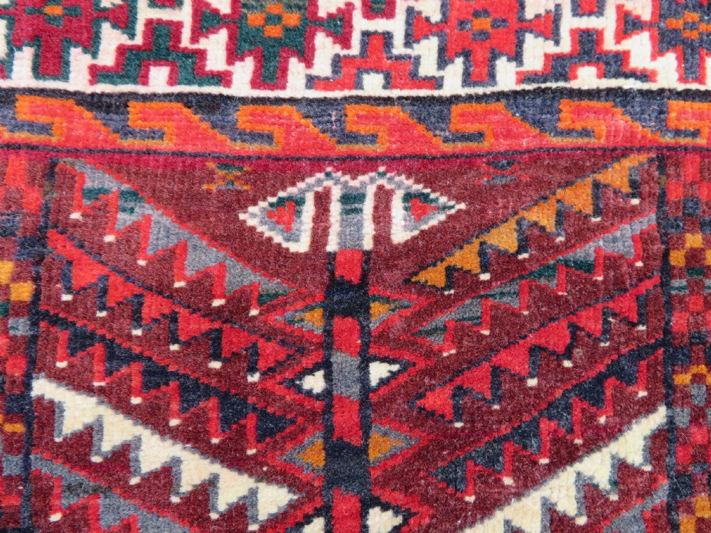 An antique woven Yomut Turkmen chuval rug in deep red wool featuring nine central geometric gul motifs surrounded by a patterned border and a detailed lower elem panel. View VIII